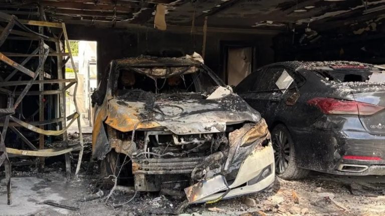 Burned vehicles sit inside a severely fire-damaged garage, with extensive structural and vehicle damage