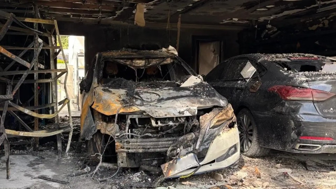 Burned vehicles sit inside a severely fire-damaged garage, with extensive structural and vehicle damage