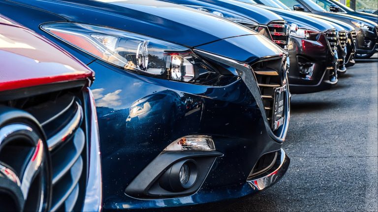 Row of shiny cars lined up at dealership showing front ends
