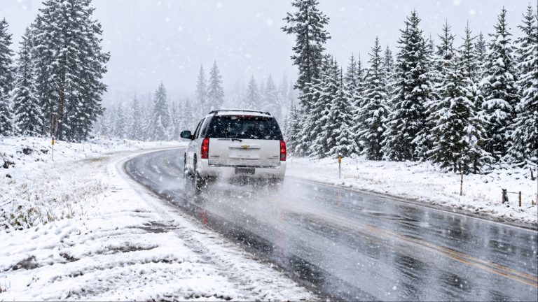 White SUV driving on snowy road through forest in winter