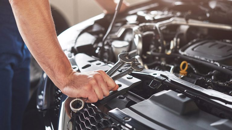 Mechanic holding wrenches over open car engine bay for maintenance