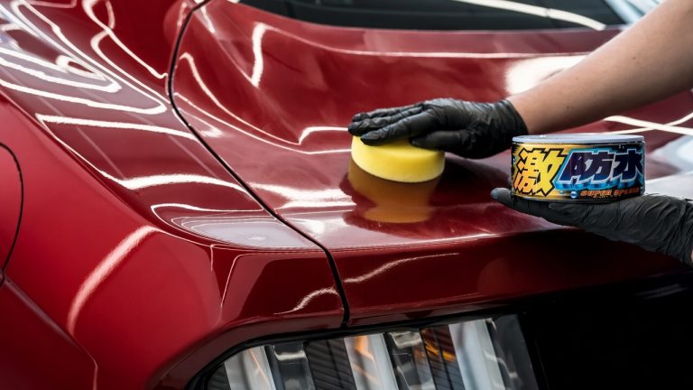 Car wax being hand-applied to a red vehicle’s glossy paint for added shine and protection