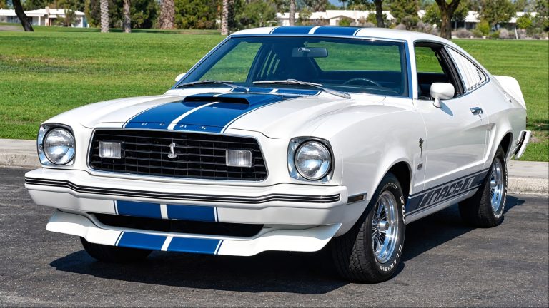 White Ford Mustang II Mach 1 with blue racing stripes, parked outdoors