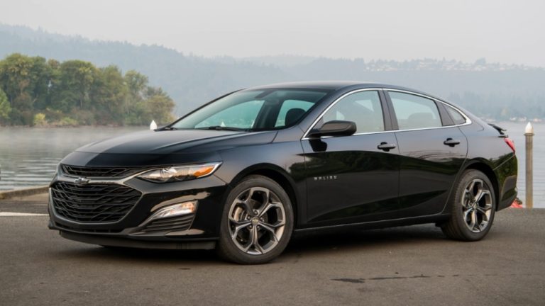 Chevrolet Malibu parked beside a peaceful lakeside, with mountains and trees in background