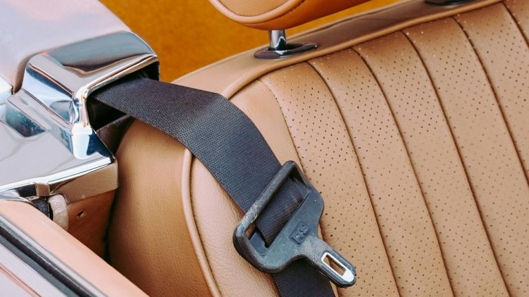 Close-up of a classic car’s seatbelt buckle resting on perforated leather upholstery