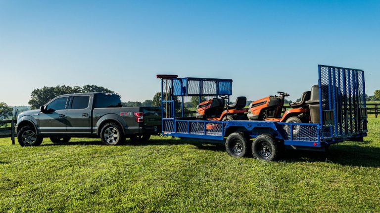 Ford F-150 towing a utility trailer loaded with two orange riding mowers