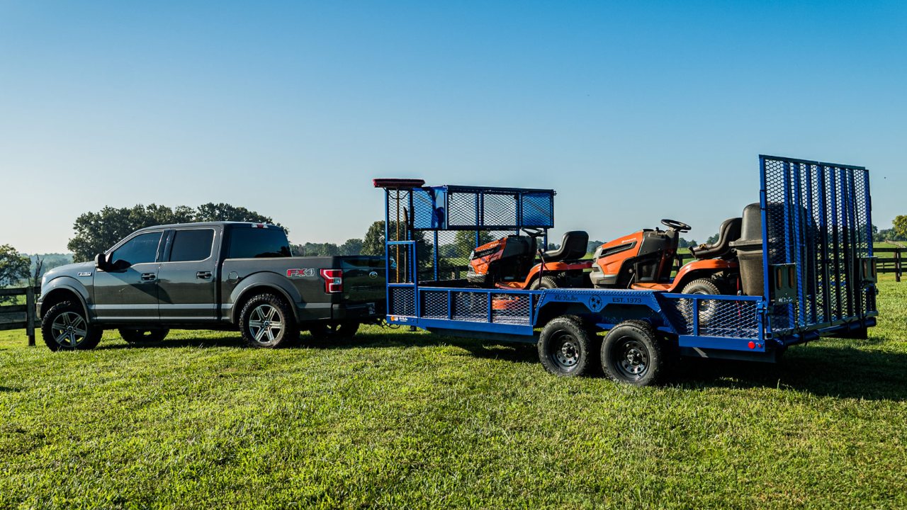Ford F-150 towing a utility trailer loaded with two orange riding mowers