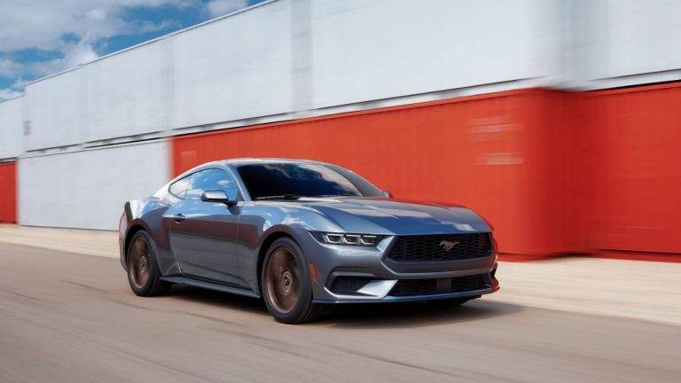 Ford Mustang driving past an industrial building under a clear sky