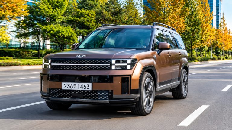 Brown Hyundai SUV drives past autumn trees on city road
