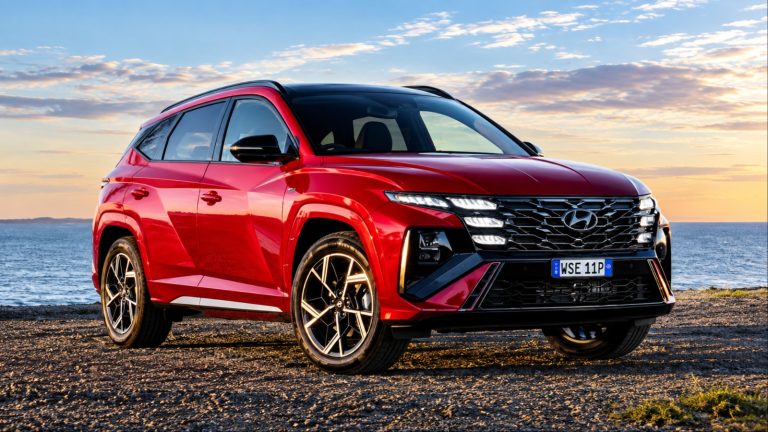 Hyundai Tucson Hybrid parked beside the coast, showcasing its bold design and striking red exterior
