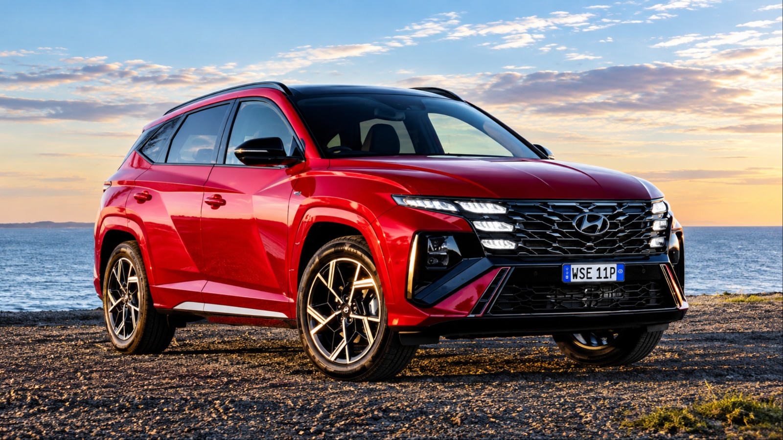 Hyundai Tucson Hybrid parked beside the coast, showcasing its bold design and striking red exterior