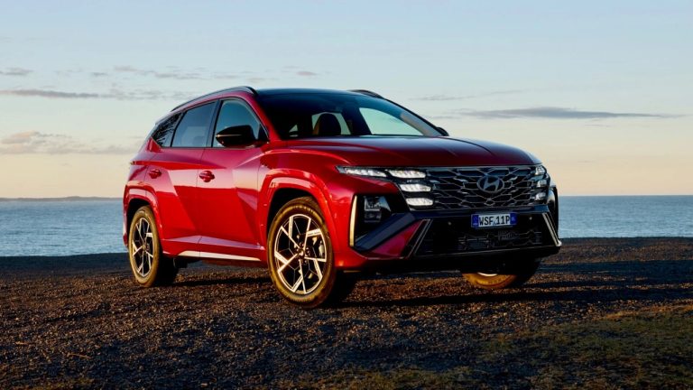 Hyundai Tucson shown in red, parked beside the coast under an evening sky