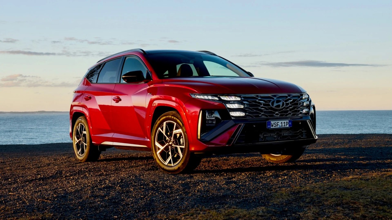 Hyundai Tucson shown in red, parked beside the coast under an evening sky
