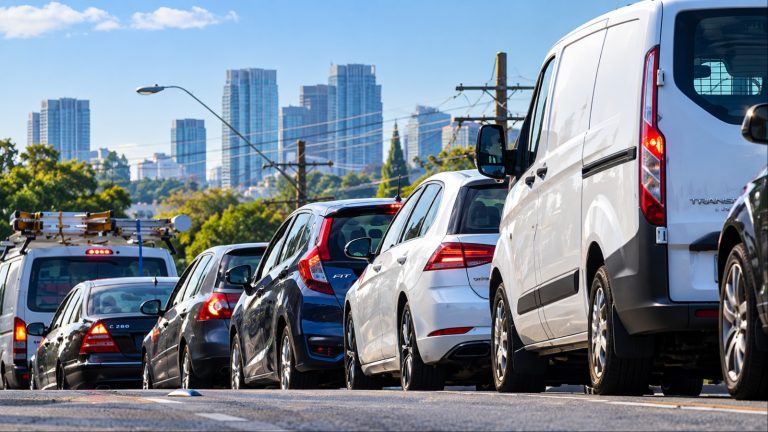 Vehicles queued in traffic on road near city skyline under blue sky