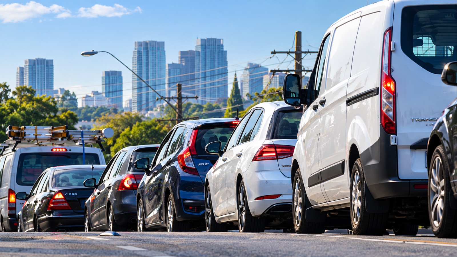Vehicles queued in traffic on road near city skyline under blue sky