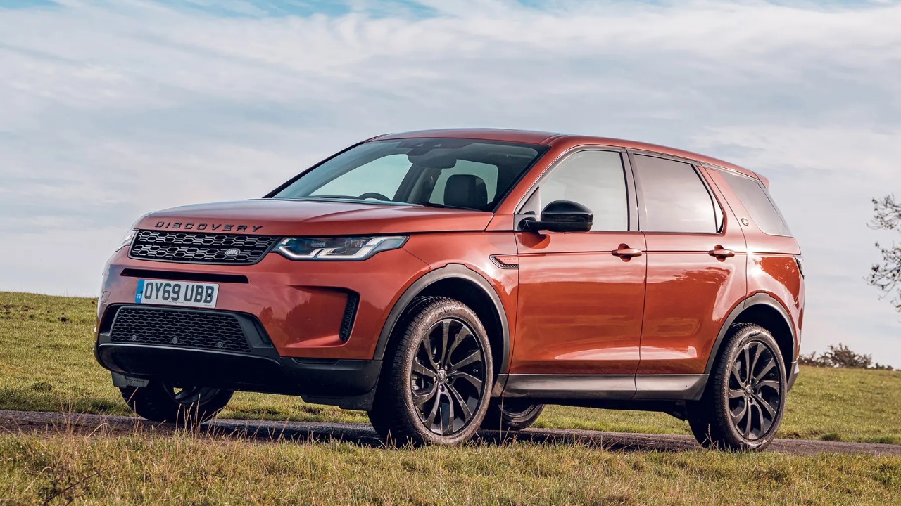 Land Rover Discovery Sport parked on a grassy hillside beneath a bright sky