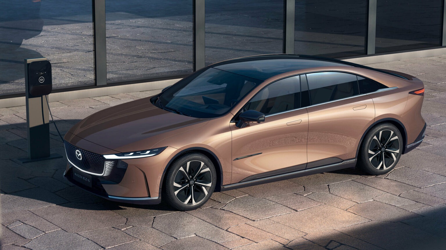 Sleek copper Mazda EZ-6 electric sedan parked by EV charger