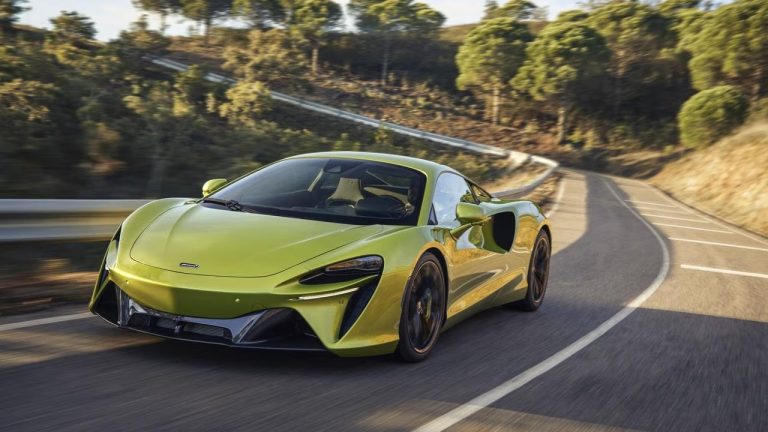 McLaren sports car speeds along a winding mountain road surrounded by trees