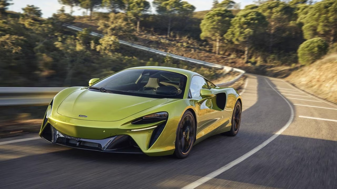 McLaren sports car speeds along a winding mountain road surrounded by trees