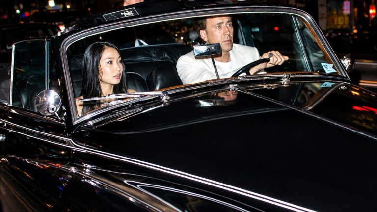 Nicolas Cage driving a classic black convertible