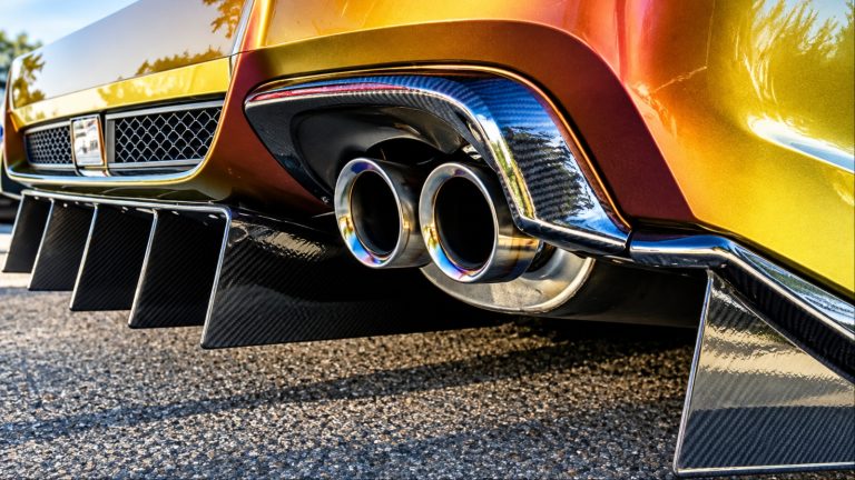Orange car with dual exhaust pipes on concrete.