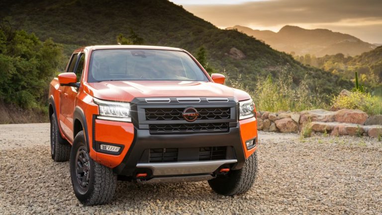 Orange Nissan Frontier parked on a rocky trail with mountains in background
