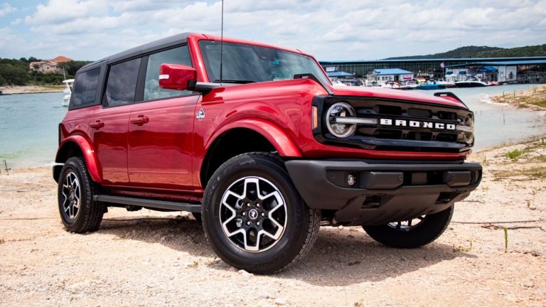 Red Ford Bronco parked beside the water under bright summer skies