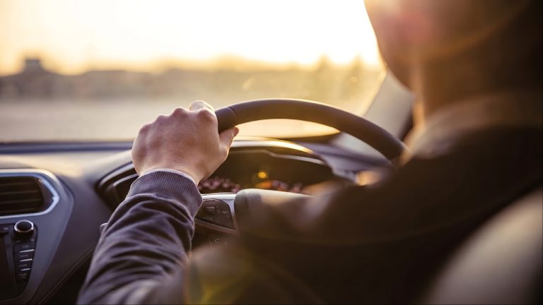 Driver holding a steering wheel during sunset with bright light
