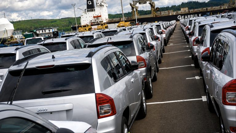 Silver Jeeps in long rows at port near cargo ship