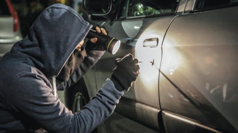 Thief inspecting a parked car at night, highlighting the risk of vehicle theft