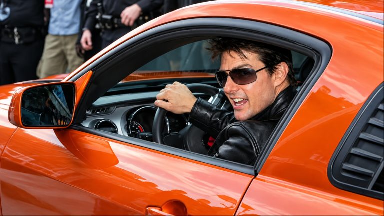 Tom Cruise smiling in orange sports car with sunglasses on
