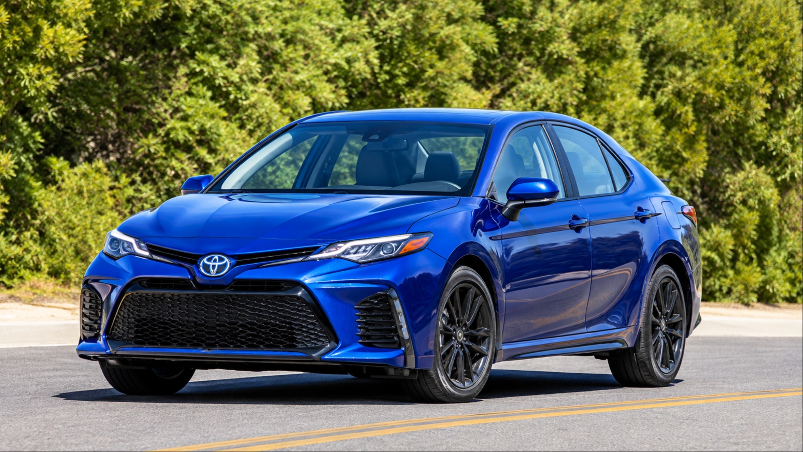 Blue Toyota sedan with black wheels on sunny road