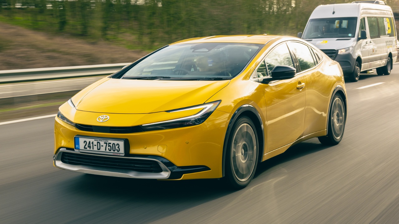 Toyota Prius cruising on the highway with a van following closely behind