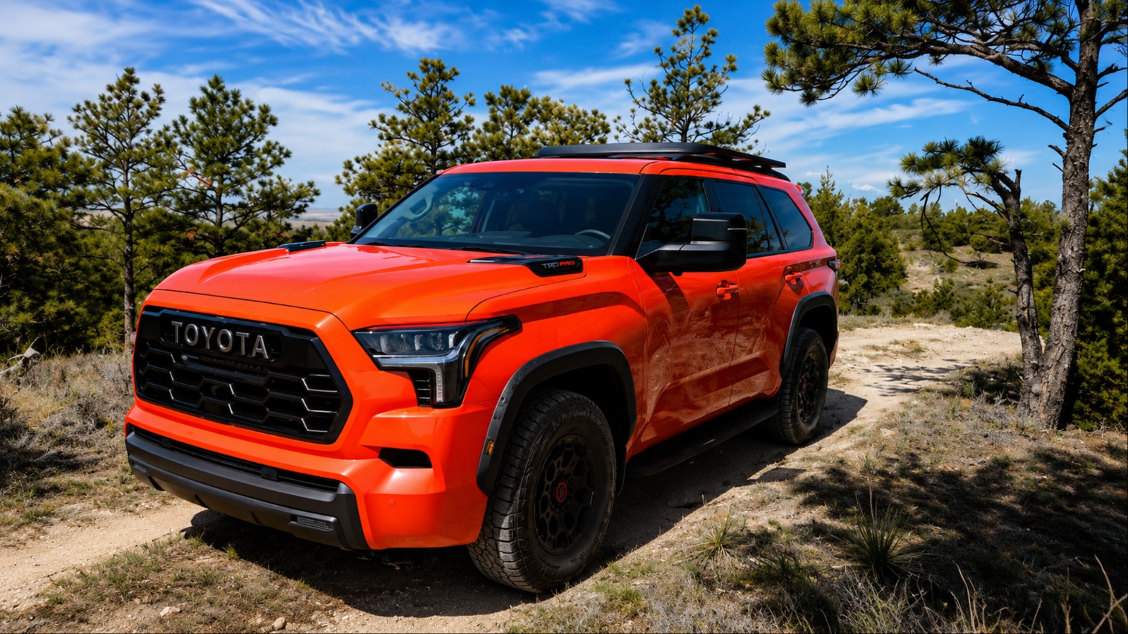 Bright red Toyota Sequoia parked on a rugged forest trail under blue skies