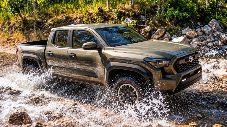 Toyota Tacoma crossing a rocky stream, splashing through water on an off-road trail