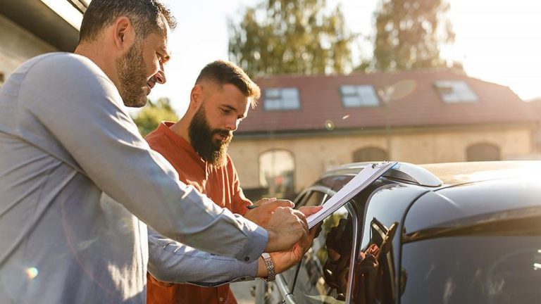 Two people review a vehicle’s warranty paperwork beside the car