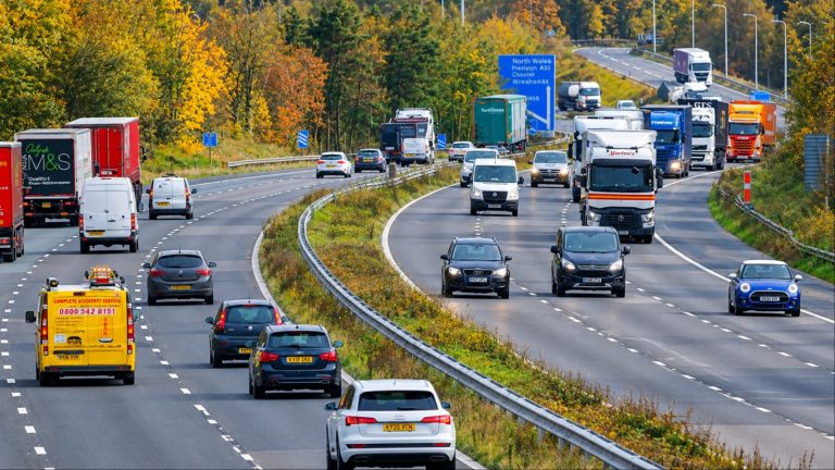 Busy highway traffic with cars trucks vans under autumn trees