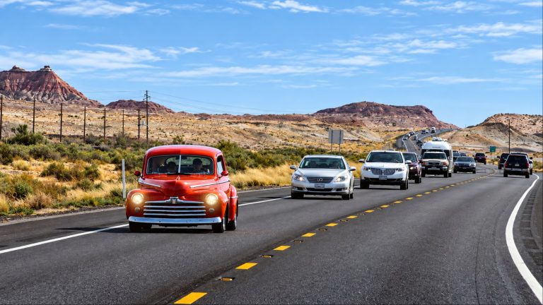 Vintage car leading traffic on a highway through a rugged desert landscape
