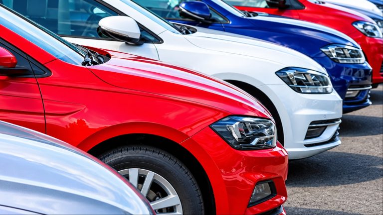 Row of colorful new cars parked in outdoor dealership lot.