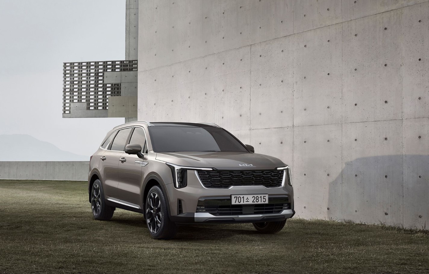 2027 Kia Sorento Hybrid parked beside modern concrete architecture, highlighting its bold grille and sleek SUV design
