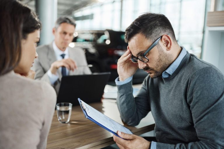 Worried car buyer reviewing purchase paperwork at dealership