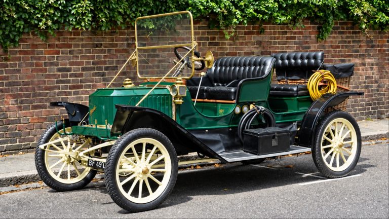 Vintage green classic car with brass details parked by brick wall