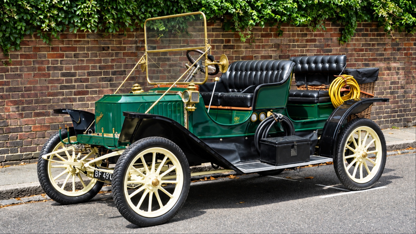 Vintage green classic car with brass details parked by brick wall