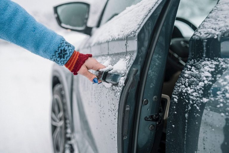 A driver scrapes snow and ice from a frozen car door during winter