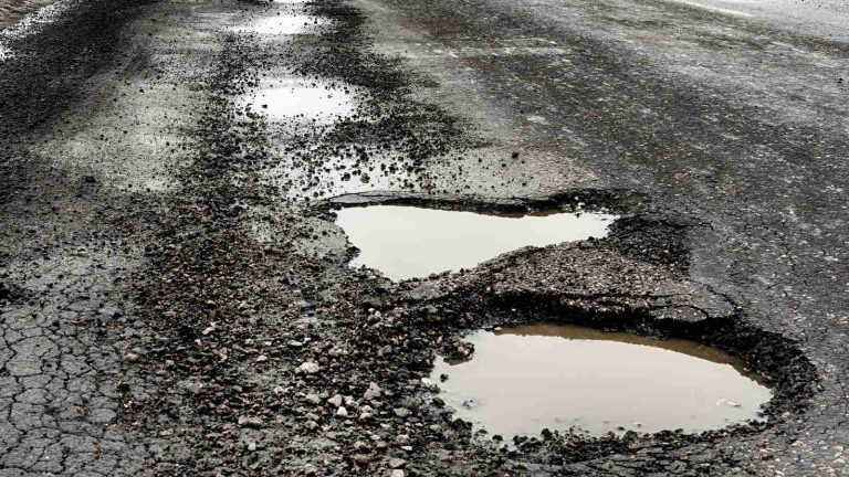 A severely damaged road surface filled with large potholes and standing water