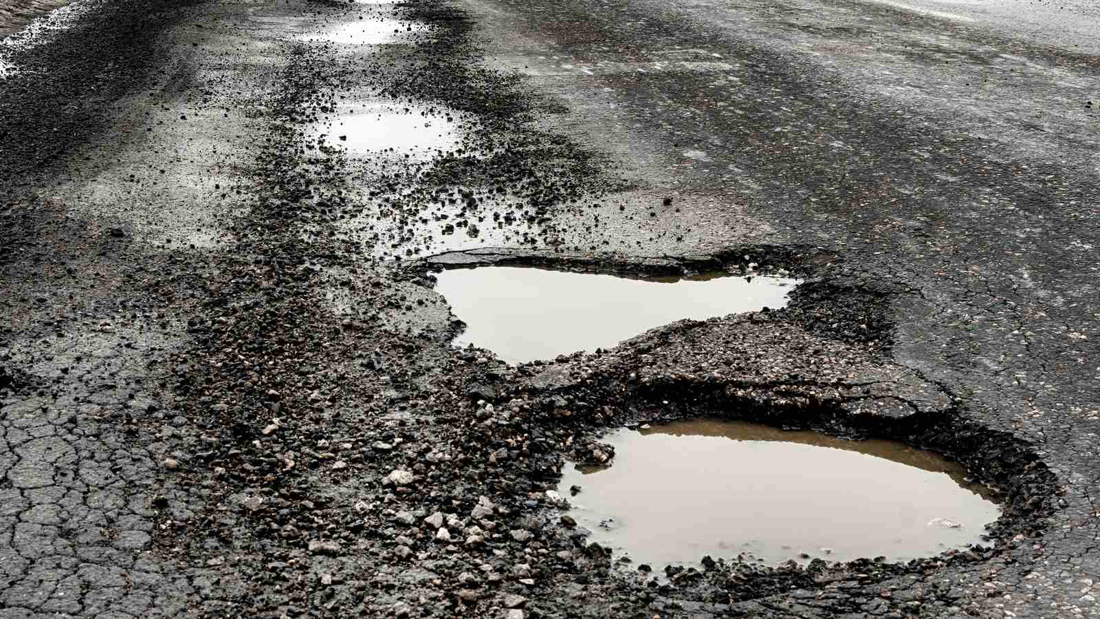 A severely damaged road surface filled with large potholes and standing water