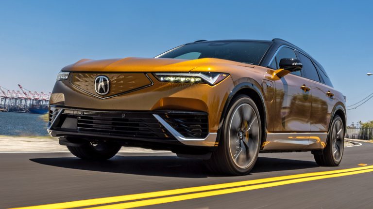 Acura ZDX electric SUV driving along a coastal highway, showcasing its bold front styling
