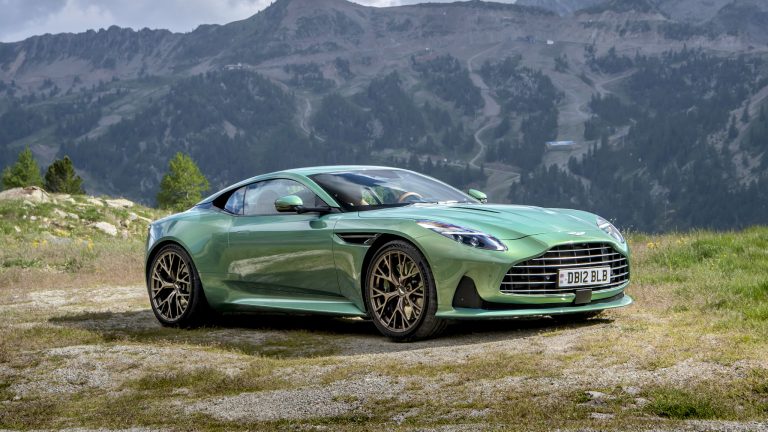 Aston Martin DB12 parked on a mountain meadow with rugged peaks behind it