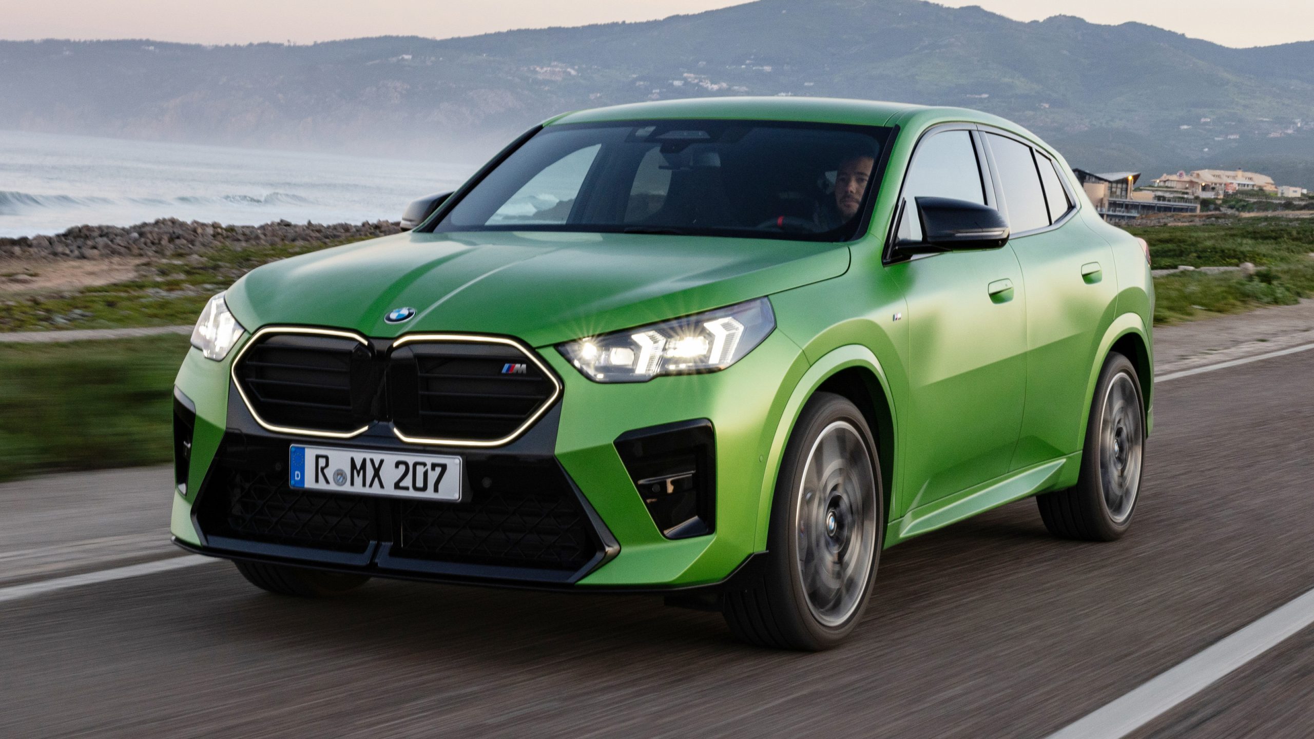 Green BMW drives along coastal road