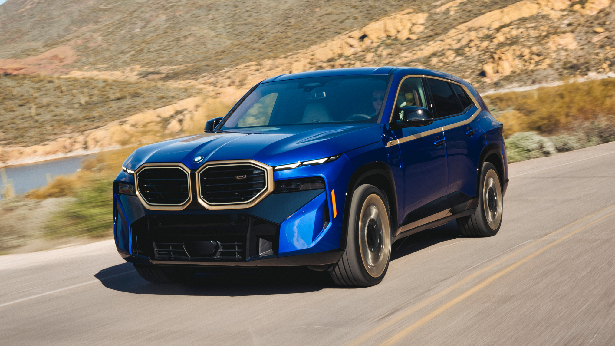 BMW XM driving along a winding mountain road, showcasing its bold grille and aggressive SUV styling